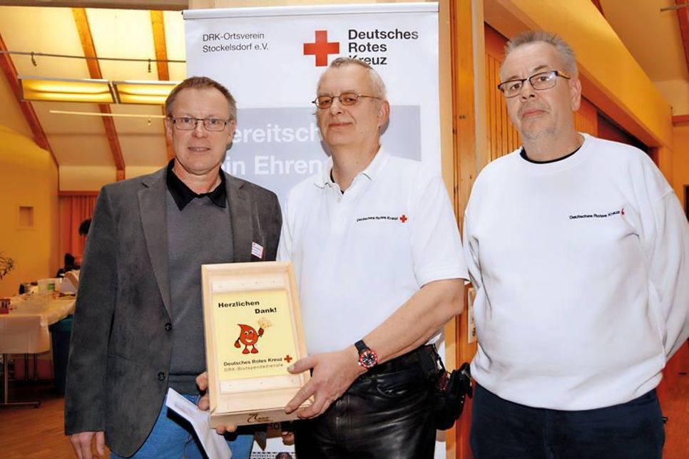 Zum Dank für die treue Spendenbereitschaft überreichen Harald Hinz vom DRK Blutspendedienst Nord-Ost (l.) mit Bereitschaftsleiter Kai Henrich (r.) Präsente an den Jubilar.  (Foto: Setje-Eilers)