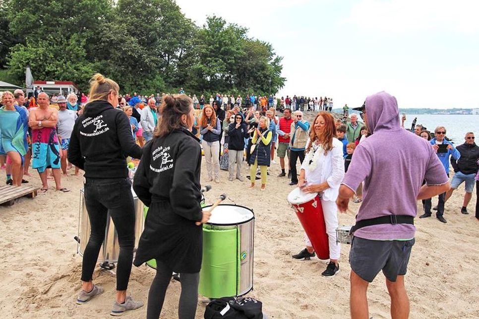 Die Samba Percussionformation spielt auf. Zuschauer verfolgen das bunte Treiben am Strand.