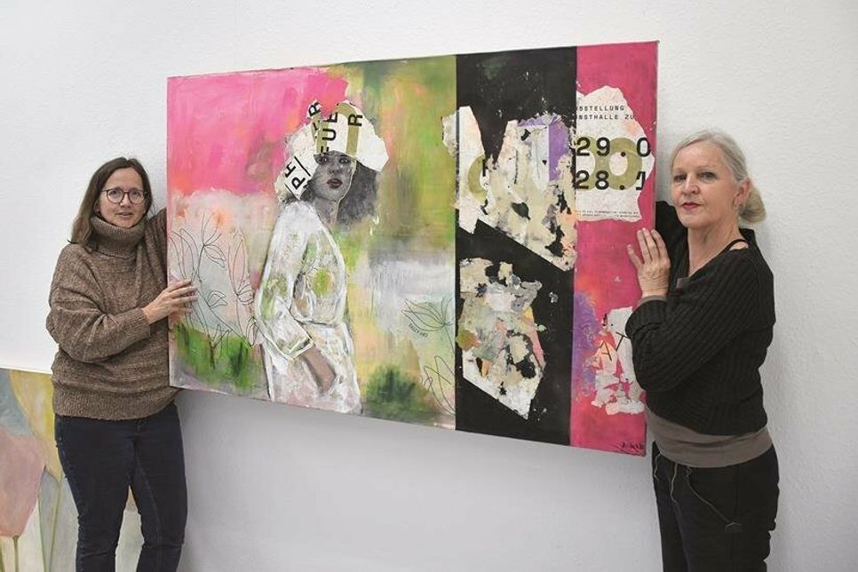 Dr. Heidi Schooltink (links) und Wübke Rohlfs-Grigull hängen eines der größten Bilder der Ausstellung: Diese Acryl-Mix-Collage von Britta Kähler ist mit „Tally-Ho“ betitelt.