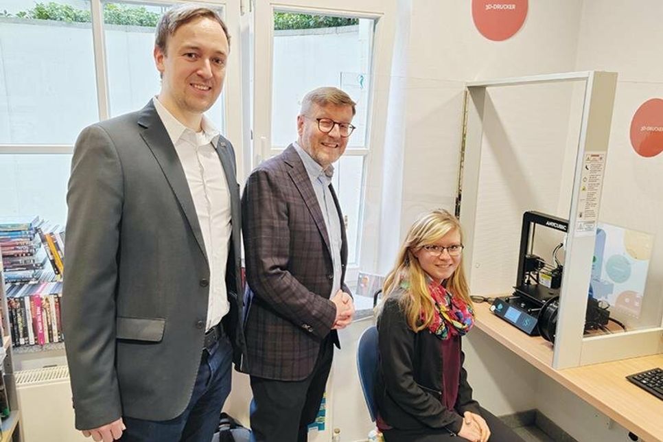 Celina Matschall (sitzend) und Florian Weber von der Staatskanzlei Abteilung Digitalisierung und zentrales IT-Management (links) mit Bürgermeister Sven Partheil-Böhnke vor dem 3D-Drucker.