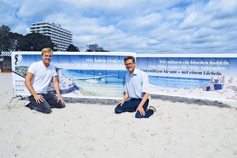Friedrich Flüh von der TSNT GmbH und Tourismuschef Joachim Nitz weisen auf die Arbeiten am Strand hin: „Wir haben Großes vor und müssen ein bisschen buddeln. Unterstützen Sie uns bitte mit einem Lächeln.“ (Foto: René Kleinschmidt)