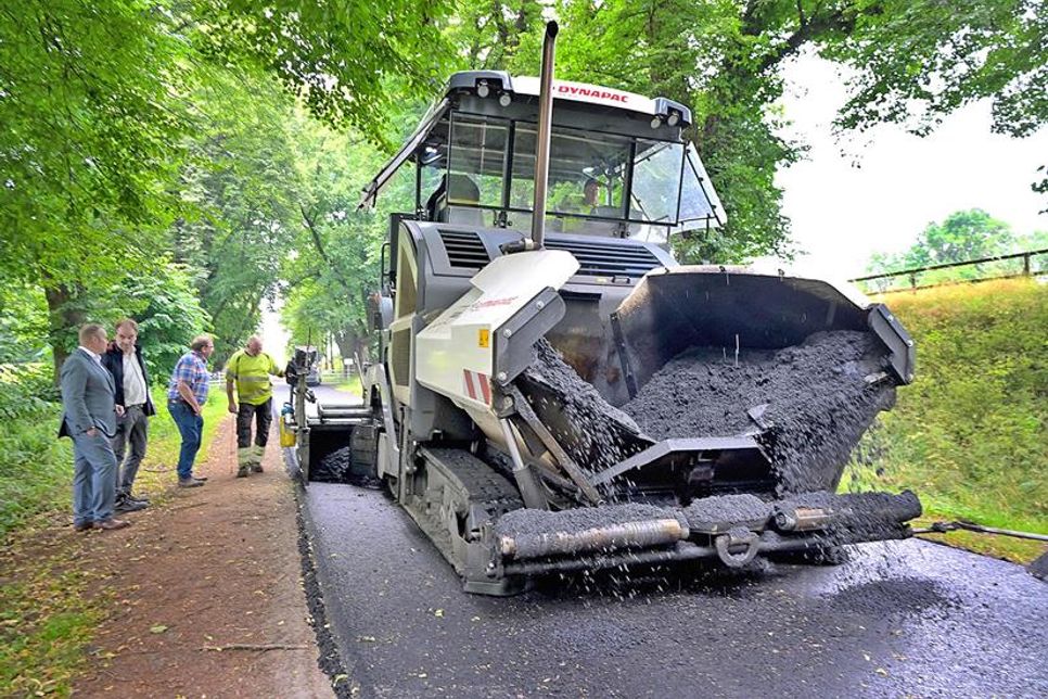 Das heiße Mischgut wird regelmäßig durch Themo-Lkw angeliefert und mit dem Baufahrzeug verteilt – dabei wird die Straße ein bisschen höher und breiter, so dass in der anschließenden Nachbereitung die Bankettstreifen aufgefüllt werden müssen.