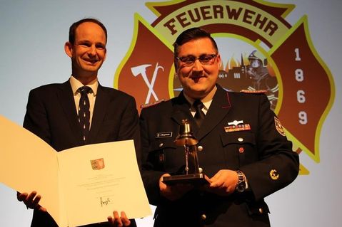 Staatssekretär Torsten Geerdts (lks.) überreichte Gemeindewehrführer Alexander Wengelewski eine Ehrenurkunde und eine goldene Glocke.