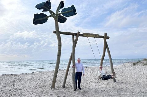 „Auf die Schaukel, fertig, los!“: Jacqueline Schumacher vom Tourismus-Service Grömitz und Manfred Wohnrade zeigen am neuen Standort an der Wiese Uferstraße, wie viel Spaß die beliebte Grömitz-Schaukel mit Ostseeblick macht.